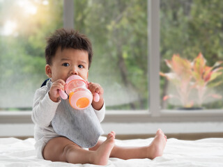 Cute little Asian boy drinking orange juice from the training bottle with straw.