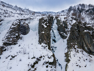 aerial drone shot of frozen waterfall in natural mountain landscape with snow in winter