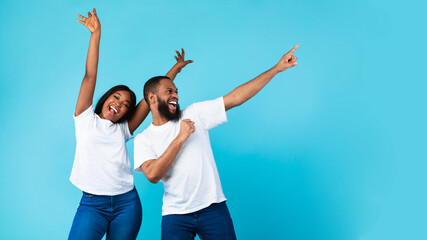Smiling black couple celebrating win, pointing aside at copy space