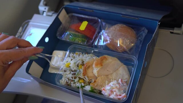 Closeup view 4k stock video footage of woman eating food on board of flying plane. Paper box full of plastic trays with different food: rice, chicken, salad, cucumbers, tomatos, bun and butter packed