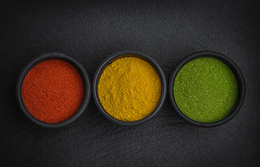 Obraz na płótnie Canvas Herbs and spices for cooking on black stone plate. Paprika, turmeric and dried bay leaf. Look like traffic lights .