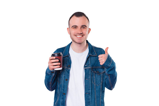 Photo of cheerful handsome man wearing jeans jacket holding cup of coffee and showing thumb up