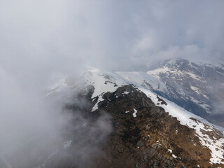 aerial drone shot in natural mountains landscape with snow in winter. cloudy day with fog. italian alps. trekking trail with people hiking, alternative safe sport during covid pandemic