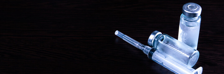 2 doses of Sars-Kov-2 coronavirus vaccine in transparent glass ampoules, covered with frost and a disposable syringe, on a dark background, short focus, toning