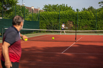 Fototapeta premium Pensioners playing tennis outside on the clay tennis court, active seniors, sport concept