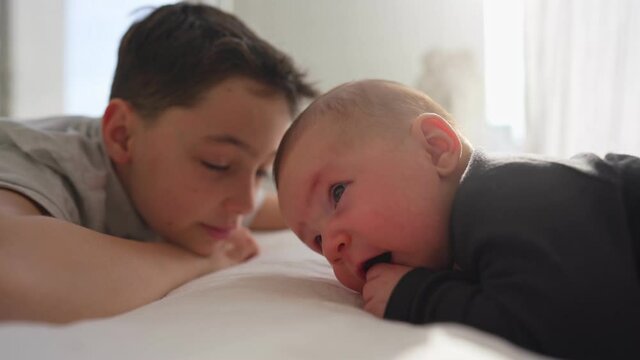 Happy little brother with newborn baby lying in a bed together, kissing and hugging. New born baby and three years old brother together. Love. Family. High quality 4k footage