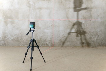 The laser level projects red lines onto the wall with a rough finish