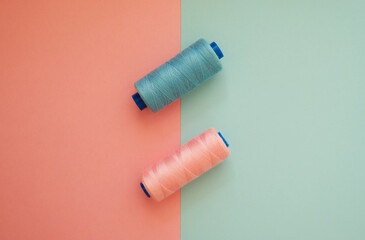 Pink and blue sewing thread bobbins on geometric two-color background. Textile or handicraft concept