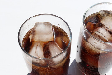 Two glasses of cola with ice cubes on white table background. Top view, copy space. Hard light, shadow.  Refreshing summer drink