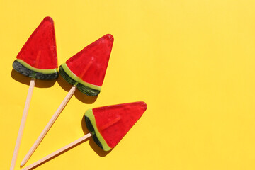 Watermelon popsicle on colored backdrop. Bright summer background. Lollipop in piece of watermelon shape. Candy on stick. Top view, Copy space. Hello summer composition on yellow background flat lay
