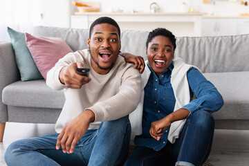 Excited black couple spending weekend together watching tv