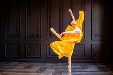 elegant ballerina in pointe shoes dances with flowing yellow fabric on a dark gray background