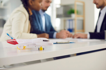 Travel, flight and health insurance. Closeup airplane model on desk and multi-ethnic couple signing...