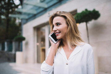 Positive woman talking on smartphone near modern building