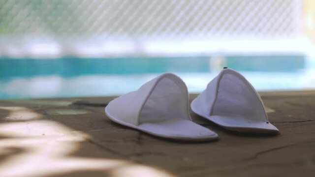 white cloth carpet sippers placed on the side of a out of focus pool with light reflections playing in the distance showing the luxury and relaxation of a expensive resort spa in rajasthan india