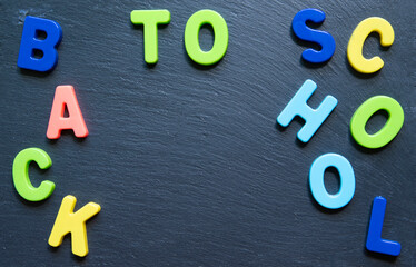 Lettering back to school. Frame from multicolored letters on black stone background. Topview. Copyspace.
