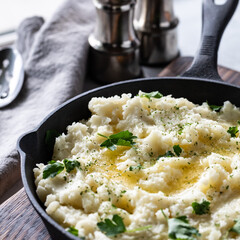 Close up of a cast iron skillet frypan filled with mashed potatoes and topped with melted butter and parsley pieces.