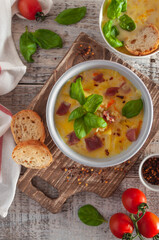 Vegetable bright yellow soup with ham and basil in a round bowl on a wooden background