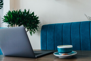 Modern laptop with a phone and a cup of matcha coffee in a large cup on a wooden table. Stylish cafe