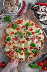 Pizza with sausage, mushrooms and cheese on a wooden gray background, a piece of which is pulled by a child's hand