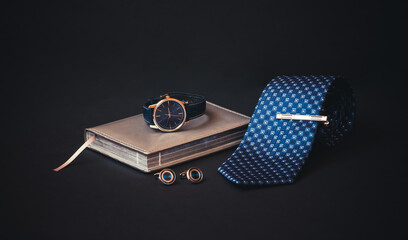 Rolled necktie, stylish tie pin, cufflinks, diary and watch.  Selective focus.