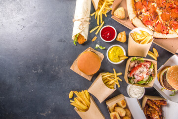 Delivery fastfood ordering food online concept. Large set of assorted take out foods pizza, french fries, fried chicken nuggets, burgers, salads, chicken wings, sides, black concrete background