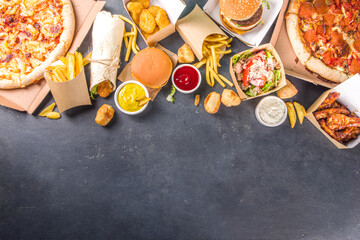 Delivery fastfood ordering food online concept. Large set of assorted take out foods pizza, french fries, fried chicken nuggets, burgers, salads, chicken wings, sides, black concrete background - obrazy, fototapety, plakaty
