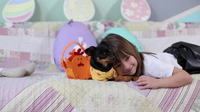 Adorable little girl hug her pet at home on sofa. Kid preparing for Easter at home during quarantine. Cute dog