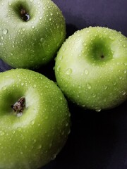 Granny smith apples with water drops on a black surface.