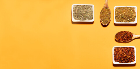 Collection of three spices on wooden spoons and white bowls on orange background,top view.Space for text