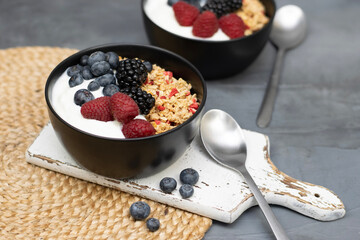 Muesli with yougurt and fresh berries in black bowl on dark gray background.