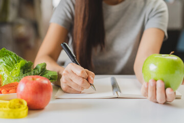 Diet, Dieting young asian woman working, write diet plan right nutrition, hold green apple, vegetables salad is food for good health not choose eat junk food. Nutritionist female, Weight loss person.