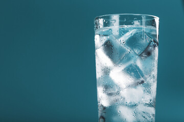 Ice cubes in a glass with crystal clear water on a blue background.