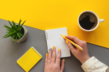 Female hands writing on notepad. Office table desk trendy yellow and grey colors. Workplace with...