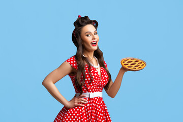 Happy pin up woman in polka dot red dress holding homemade sweet pie on blue studio background