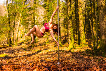 Exercises of a Caucasian acrobat dancing pole dance in the forest in autumn. Circus stunts in nature