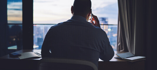 Crop businessman talking on smartphone in office at dawn