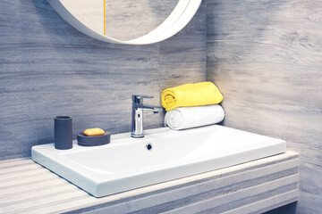 Luxury faucet mixer and white towel on a white sink in a beautiful gray bathroom. Sanitary...