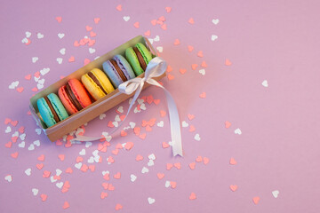Multicolored macarons in a paper box and multicolored sweets on a romantic background.
