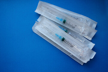 Syringes with a needle in the package lie on a blue background. Vaccination. The concept of...