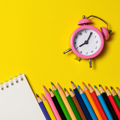 Fototapeta na wymiar Pink alarm clock with office supplies on yellow background.