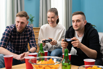 Multinational friends sitting at home on couch and playing video games on console. Cheerful woman having fun winning over man in game.