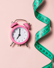 Pink alarm clock with teal measuring tape, top view. Healthy lifestyle, weight loss.