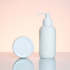 Hand cream in a bottle and jar on a light pink background with reflection.