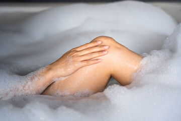 Action of woman hand is patting on the leg for clean skin during taking spa massage in foaming bathtub. Healthcare, skincare and beauty relaxation activity concept photo.