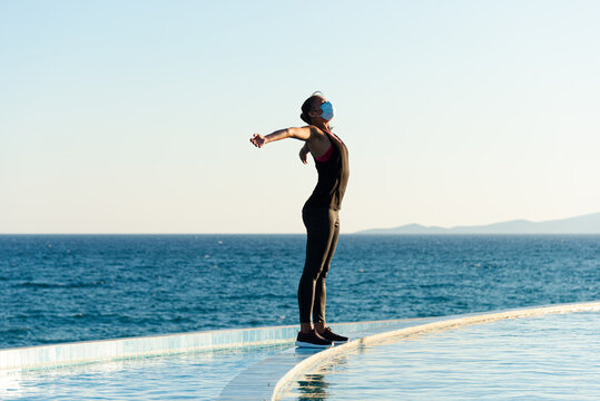 Young woman with protective surgical face mask performing yoga stretching exercises outdoor during covid-19 coronavirus pandemic