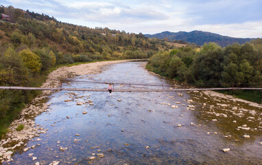 Beautiful woman in hat and dress walk on wooden bridge across mountain river. Aerial top view, travel concept