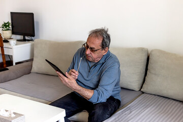 Caucasian senior man using a home test kit for coronavirus in his home. Elderly man using a cotton swab up his nose. Mature man getting online medical help and advice during video call with doctor.