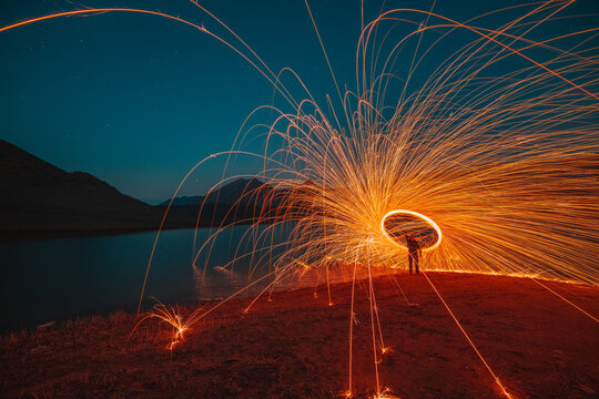 Fire show, swirl, steel wool. Sparks from a metal on the lake and mountais. Night landscape with light effects.