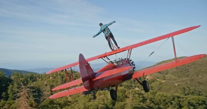 Stuntman rides on top of plane over forest, aerial
